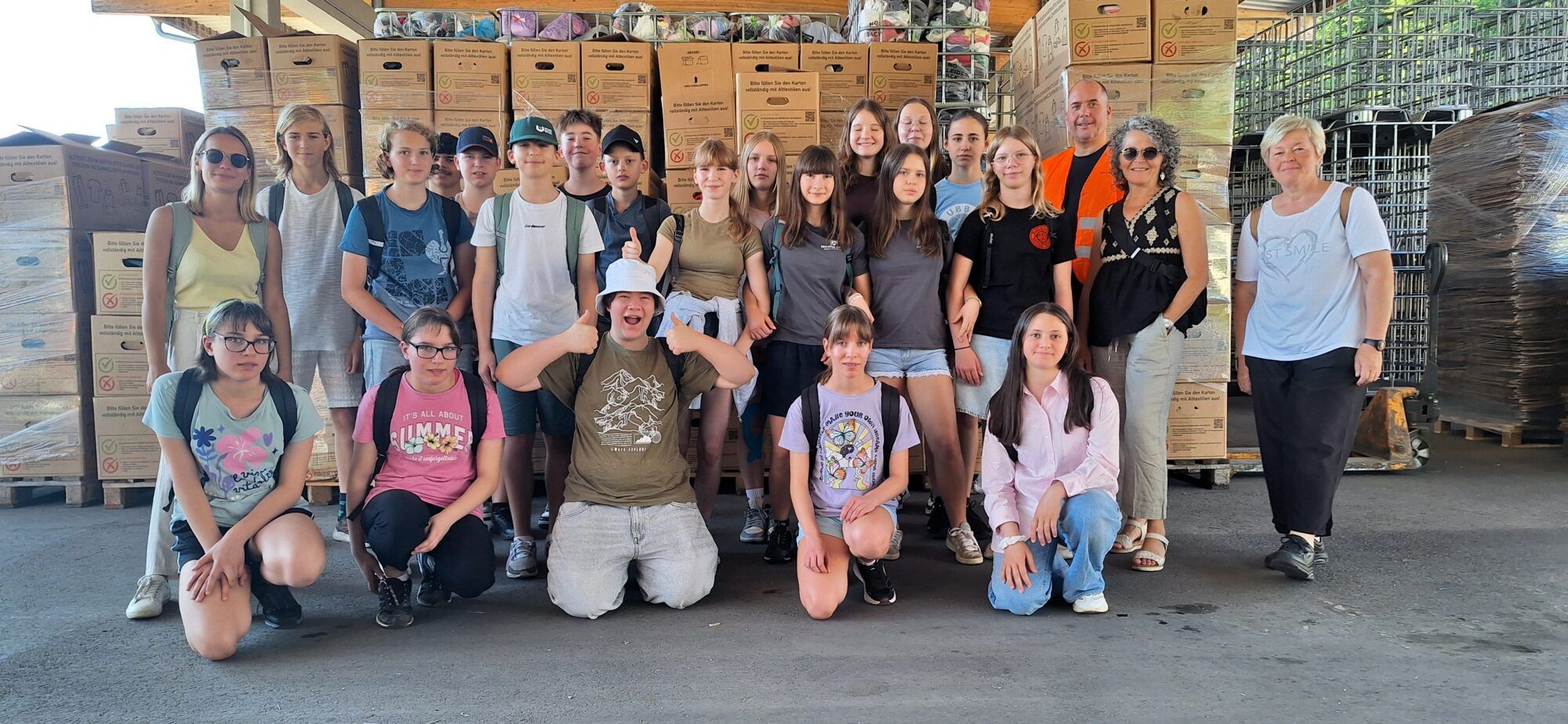 Auf dem Foto sind erwachsene Personen und Kinder der Mittelschule in einer Recyclinghalle
