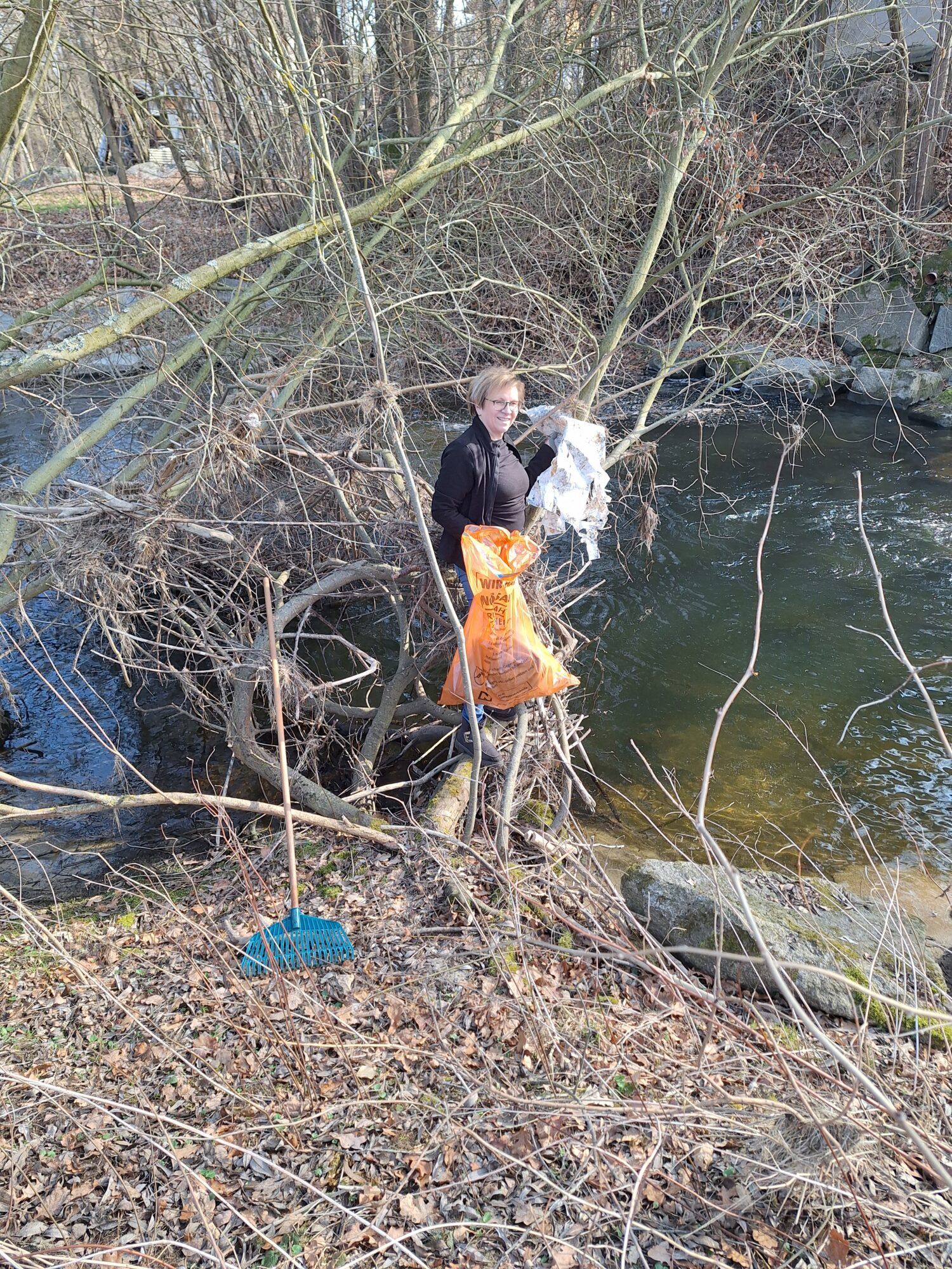 Eine Frau beim Einsammeln von achtlos weggeworfenen Abfall am Bachufer