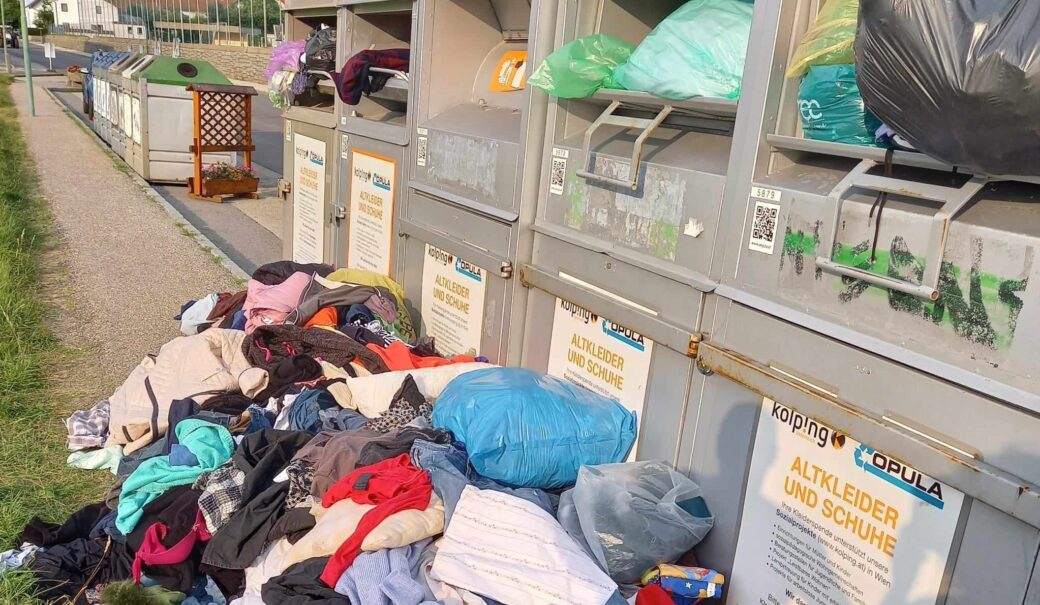 Altkleidercontainer mit davor achtlos weggeworfenen Kleidungsst&uuml;cken